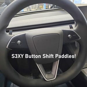 Może przedstawiać: Czarna skórzana kierownica z srebrnymi akcentami i dwiema łopatkami zmiany biegów z przyciskami, oznaczonymi znakami plus i minus. Tekst "S3XY Button Shift Paddles!" jest widoczny na zdjęciu.