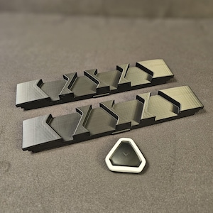 Könnte beinhalten: Zwei schwarze Plastik-Organizer mit mehreren Steckplätzen zum Aufbewahren von Kleinteilen und ein weißes dreieckiges Objekt mit schwarzer Mitte.