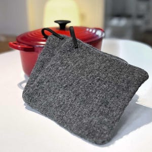 以下が含まれることがあります： 黒い革の持ち手付きの灰色の鍋つかみ2枚セット。鍋つかみは柔らかくふわふわした素材でできており、熱い鍋やフライパンから手を守るのに最適です。