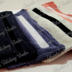 May include: A row of five rectangular, plush towels in varying colors: navy, purple, white, black, and coral. Each towel has a contrasting stripe. The towels are arranged diagonally, with the navy towel in the foreground.