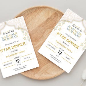 May include: Two white invitation cards with gold and blue accents. The cards announce an Iftar Dinner for Ramadan Mubarak, hosted by The Hussain Family on Wednesday, March 12th at 4 PM. The cards feature a decorative design with stars and an archway.