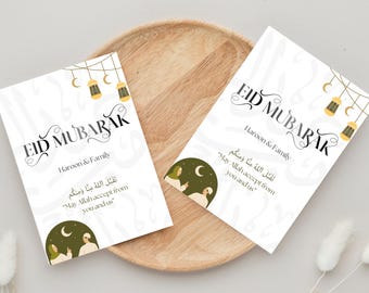 May include: Two white cards with the text "Eid Mubarak" in black calligraphy. The cards feature a green and white illustration of two people standing under a crescent moon and stars. The text "Haroon & Family" is printed below the greeting. The Arabic text "تَقَبَّلَ اللهُ مِنَّا وَمِنكُم" is printed below the illustration. The text translates to "May Allah accept from you and us."