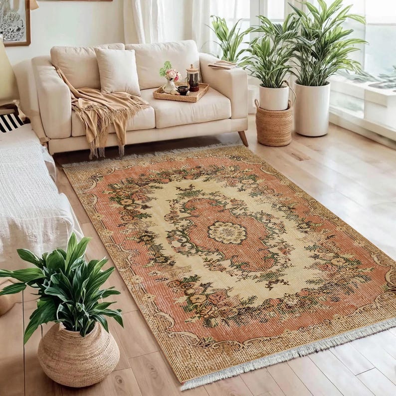 May include: A rectangular, vintage-style rug with a floral pattern in shades of peach, cream, and green. The rug features a central medallion design and a distressed appearance, adding to its antique aesthetic. The rug is placed on a hardwood floor.