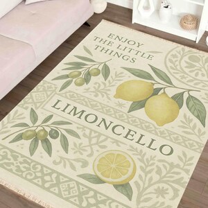 Pode incluir: Tapete retangular creme com um design de lim&atilde;o e ramos de oliveira. O tapete apresenta as palavras "Enjoy the little things" e "Limoncello". O tapete tem detalhes em verde e amarelo.