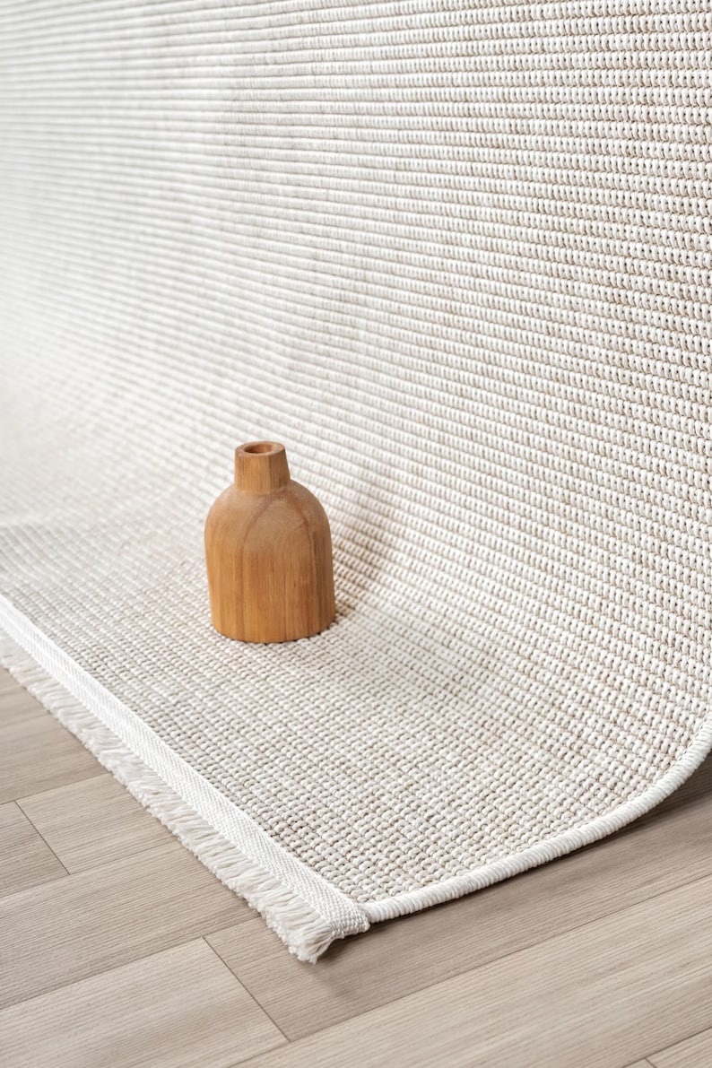 a wooden vase placed on a beige woven rug with a white fringe.