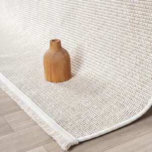 A wooden vase sits on a beige woven rug with a textured pattern.
