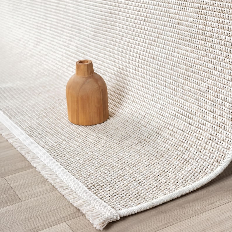 A wooden vase sits on a beige woven rug with a textured pattern.