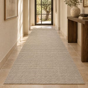 Puede incluir: Una alfombra de pasillo larga y rectangular con una textura tejida en tonos neutros beige y gris claro. La alfombra presenta un patrón de cuadrícula uniforme y ajustado en toda su superficie, extendiéndose por el suelo en un diseño plano.