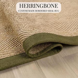 May include: A rolled sisal rug with a herringbone design and a green border. The rug features the text "HERRINGBONE CUSTOM MADE BORDERED SISAL RUG" in a white rectangular box.
