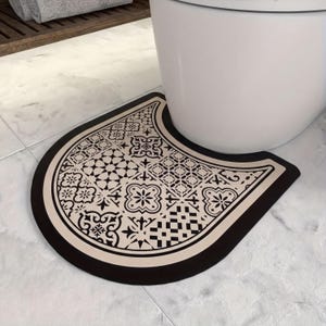 A decorative black and white patterned mat is placed on a white tiled floor next to a white toilet.
