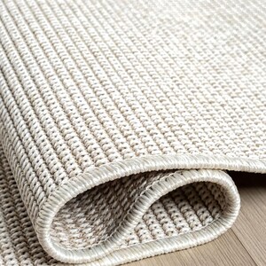 A close-up view of a beige woven rug on a wooden floor.
