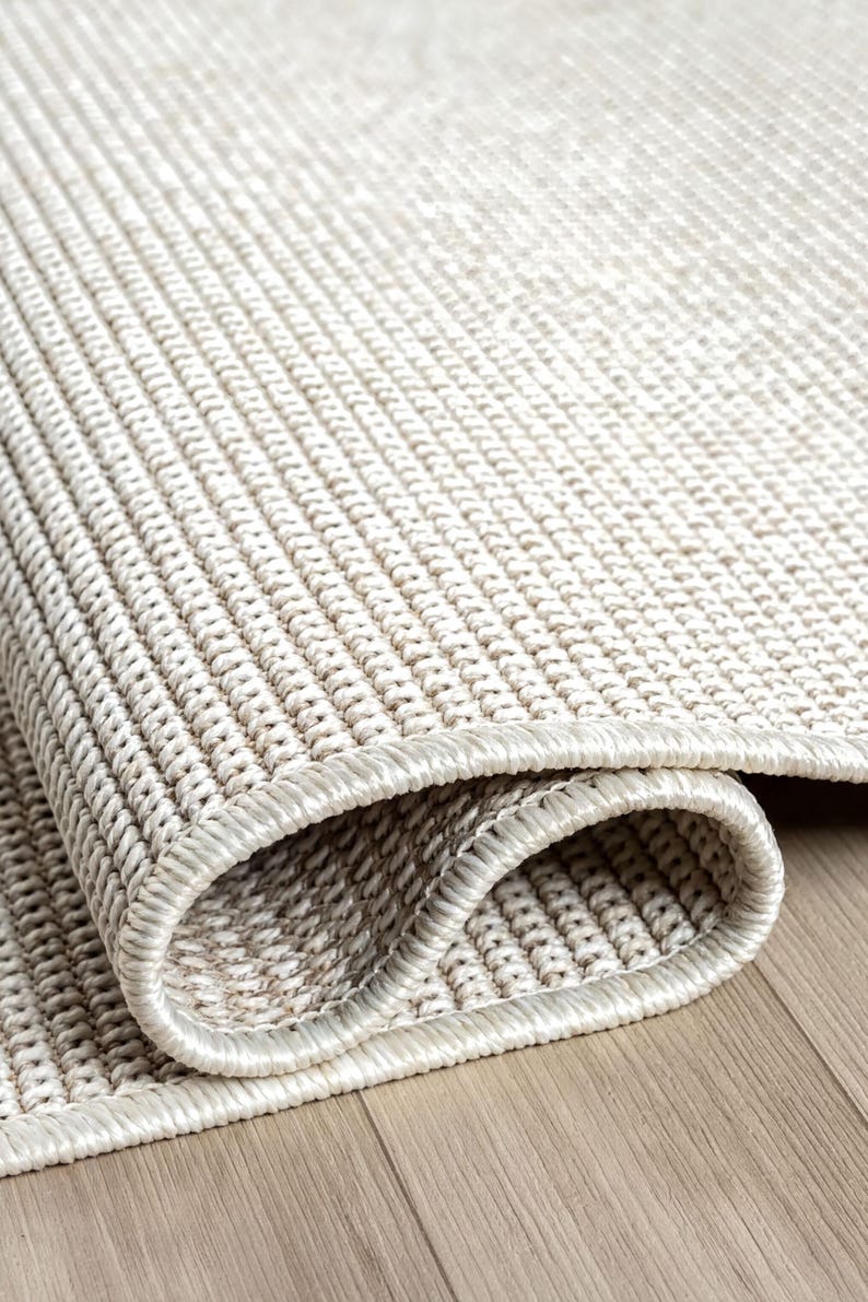 A close-up view of a beige woven rug on a wooden floor.