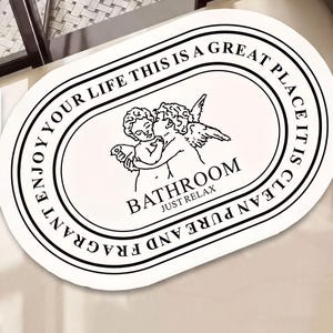 a decorative oval-shaped mat with a black and white design, including a cherub and the text "BATHROOM JUST RELAX".