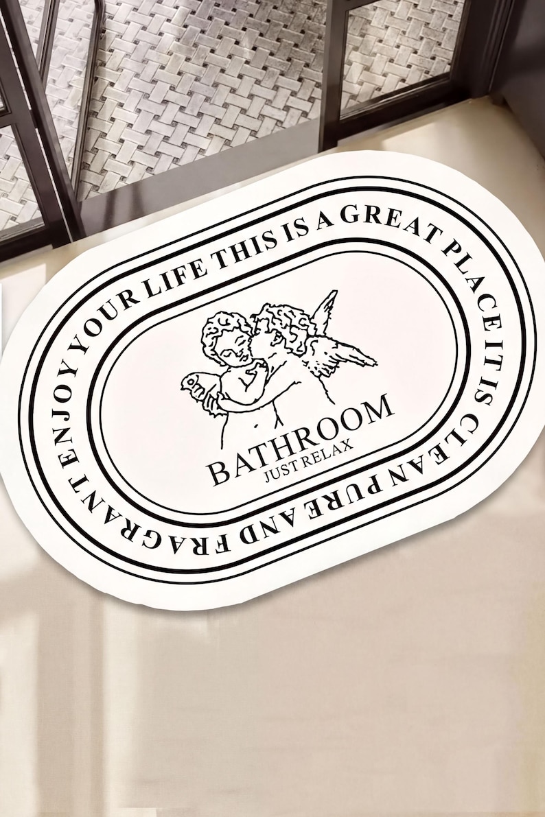 a decorative oval-shaped mat with a black and white design, including a cherub and the text "BATHROOM JUST RELAX".