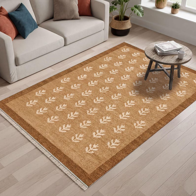 a living room with a beige sofa, a rug with a leaf pattern, and a round coffee table. There are also some potted plants and decorative items in the room.