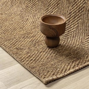 May include: A brown woven rug with a chevron design. A small wooden bowl with a rounded base is placed on the rug. The rug's texture and colour create a warm, inviting aesthetic, suitable for home decor.