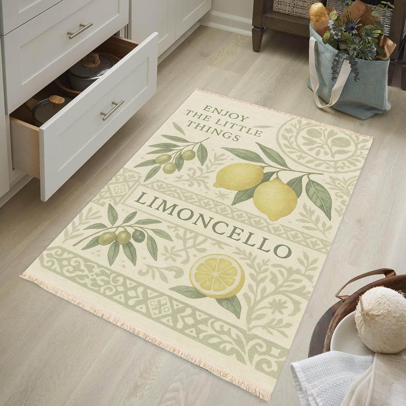 Pode incluir: Um tapete retangular com fundo creme e borda decorativa. O tapete apresenta ilustra&ccedil;&otilde;es de lim&otilde;es, azeitonas e o texto "ENJOY THE LITTLE THINGS" e "LIMONCELLO". O tapete tem uma borda com franjas.