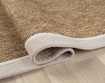 May include: Close-up of a rolled-up, woven rug with a natural, textured appearance. The rug features a light brown center and a beige border. The weave is visible, and the rug appears to be made of natural fibers.