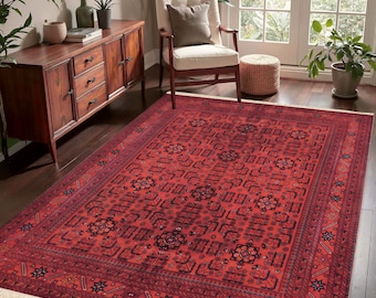 May include: A rectangular area rug featuring a deep red background with intricate black and dark blue geometric patterns, floral motifs, and a wide decorative border. The rug has short white fringe along the two shorter edges of the fabric.