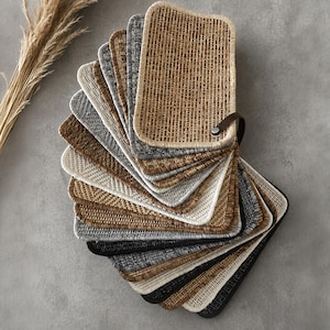 May include: A fan-shaped collection of rectangular woven fabric swatches in various neutral tones including beige, tan, gray, brown, and black. Each swatch features a distinct textured weave pattern and is bound together by a dark brown leather strap.