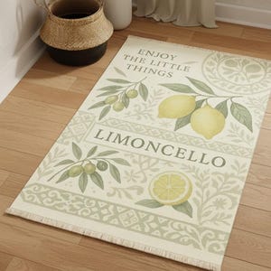Pode incluir: Tapete retangular creme com um design de lim&atilde;o e ramo de oliveira. O tapete apresenta as palavras "ENJOY THE LITTLE THINGS" e "LIMONCELLO". Possui detalhes em verde e amarelo e uma borda com franjas.