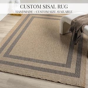 Könnte beinhalten: Ein rechteckiger, maßgefertigter Sisalteppich mit gewebter Textur und dunkelbraunem Rand. Der Teppich hat einen Fransenrand und den Text "CUSTOM SISAL RUG" und "HANDMADE - CUSTOM SIZE AVAILABLE" in Schwarz.