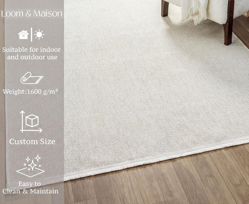a white area rug on a wooden floor, with a chair visible in the background. The rug is described as suitable for indoor and outdoor use, with a weight of 1600 g/m². It also features a custom size and is easy to clean and maintain.