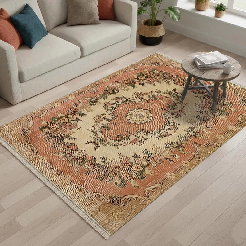 May include: A rectangular area rug with a floral pattern in shades of peach, cream, and green. The rug features a central medallion design surrounded by a border of stylized flowers and leaves. The rug has a distressed, vintage look.