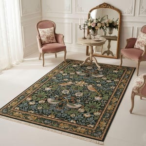 a living room with a large, ornate rug with a floral design. The room is furnished with two pink armchairs, a round wooden table, and a large mirror. There are also two vases with flowers on the table.