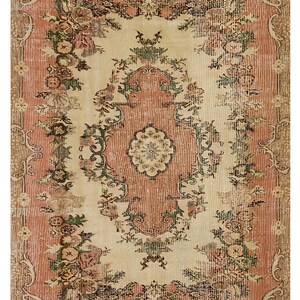 May include: A rectangular rug with a distressed, vintage look. The rug features a central cream-colored field with a floral pattern in shades of pink, green, and brown. The border is a darker brown with floral and scroll designs.
