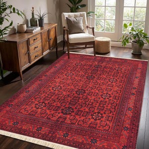 May include: A rectangular red rug with a detailed geometric pattern. The rug has a central field of repeating shapes and a detailed border. It is placed on a dark wood floor, adding warmth to the room. The rug's dimensions are in centimetres.