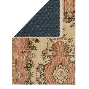 May include: A section of a vintage-style rug with a distressed floral pattern in shades of peach, cream, and olive green. The rug has a dark blue backing and a fringed edge. The design features ornate botanical motifs.