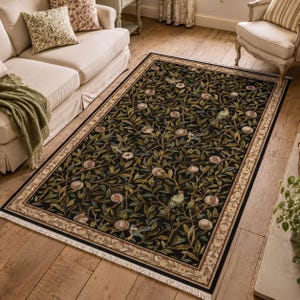 a living room with a large rug on the floor, which has a floral design. The rug is surrounded by a white sofa, a chair, and a potted plant. The room has a wooden floor and a window, creating a cozy and inviting atmosphere.