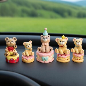 May include: Five decorative bear figurines, each perched atop a colorful cake base. The bears are tan and cream-colored, with various accessories like party hats and bows. The cakes are decorated with pink, yellow, and red frosting.