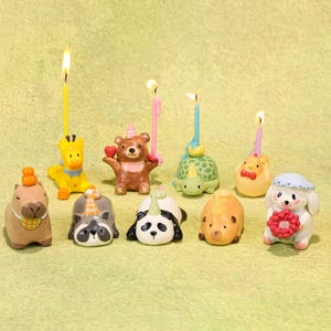 May include: A collection of whimsical animal-shaped birthday candles, including a giraffe, bear, turtle, panda, and dog, each with a lit candle. The candles are in various colors and designs, perfect for a festive celebration.