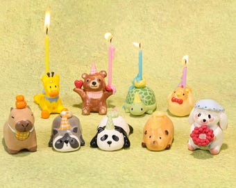 May include: A collection of whimsical animal-shaped birthday candles, including a giraffe, bear, turtle, panda, and dog, each with a lit candle. The candles are in various colors and designs, perfect for a festive celebration.