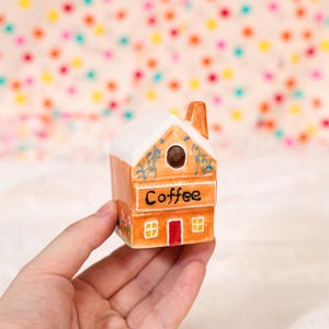 Puede incluir: Una taza de cerámica blanca con un asa negra y el texto "But First, Coffee" en negrita negra. La taza está sobre una superficie blanca. La taza mide aproximadamente 10 cm de alto.