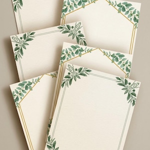 Könnte beinhalten: Eine Ansammlung cremefarbener Schreibwarenblätter, jedes mit einem Rand aus grünen Blättern und goldenen Akzenten verziert. Die Blätter im Aquarellstil verleihen dem Design eine natürliche Note. Geeignet für verschiedene Zwecke.