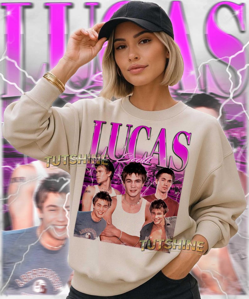 May include: Beige sweatshirt featuring a graphic of Lucas Scott in a vintage style. The design includes the name "LUCAS" in pink, with multiple images of the actor. The sweatshirt is worn with a black cap and gold bracelets.