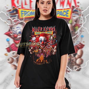 May include: Black unisex t-shirt featuring a colorful graphic of several clown faces with the text "KILLER KLOWNS FROM OUTER SPACE." The design includes a circus tent and other carnival elements. The shirt is a true-to-size fit.