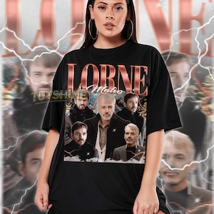 May include: Black unisex t-shirt with a graphic of a man and the text "LORNE Malvo" in a copper-coloured font. The shirt has a crew neck and short sleeves. The text "TUTSHINE" is also visible. The model is wearing a 2XL shirt.