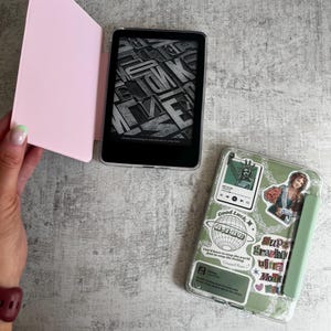 Op de afbeelding: Twee e-readers met beschermhoezen. Eén e-reader is open en toont een zwart-wit afbeelding. De andere heeft een transparante hoes versierd met stickers, waaronder de tekst "Good Luck" en "Super Graphic Ultra Mole".