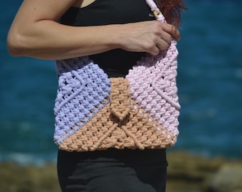 May include: A crocheted bag with a pink, purple, and beige color scheme. The bag is made with a macrame knot pattern.