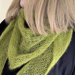 May include: A lime green knitted scarf with a lacy pattern. The scarf is made of a soft, fuzzy yarn.