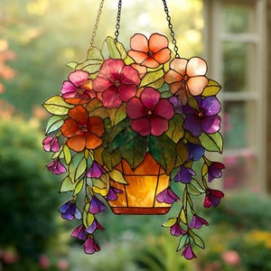 Puede incluir: Cesta colgante de vidrieras con una variedad de flores coloridas. Las flores son en tonos de rojo, naranja, rosa y morado, con hojas verdes. La cesta es de color naranja cálido y está suspendida por una cadena.