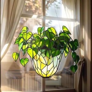 May include: A stained glass hanging planter featuring a leafy green plant design. The planter is shaped like a pot and has a yellow and green colour scheme.