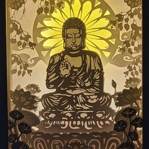 Pode incluir: Uma escultura de papel iluminada de um Buda meditando rodeado de flores de lótus e um mandala amarelo brilhante.
