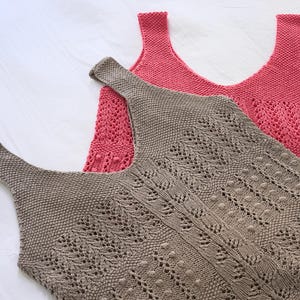 May include: Two knitted tank tops in the image. One is a muted rose color, and the other is a taupe color. The taupe tank top has a detailed openwork design. The tank tops are lying on a white surface.