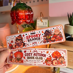 Op de afbeelding: Twee rechthoekige boekenleggers met afgeronde hoeken. De bovenste boekenlegger toont een beer met een heksenhoed, een spookje en de tekst "SPOOKY READER just one more chapter". De onderste boekenlegger toont een beer in een pompoen, een egel en "COZY AUTUMN BOOK CLUB just one more chapter".