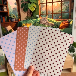 May include: Four rectangular cards with rounded corners, each featuring a distinct polka dot pattern. The colours include a light purple card with blue dots, a terracotta card with white dots, a white card with blue dots, and a white card with maroon dots.